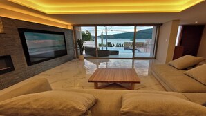 Een moderne woonkamer met een grote flatscreen televisie aan een bakstenen muur, een houten salontafel en een beige bank.