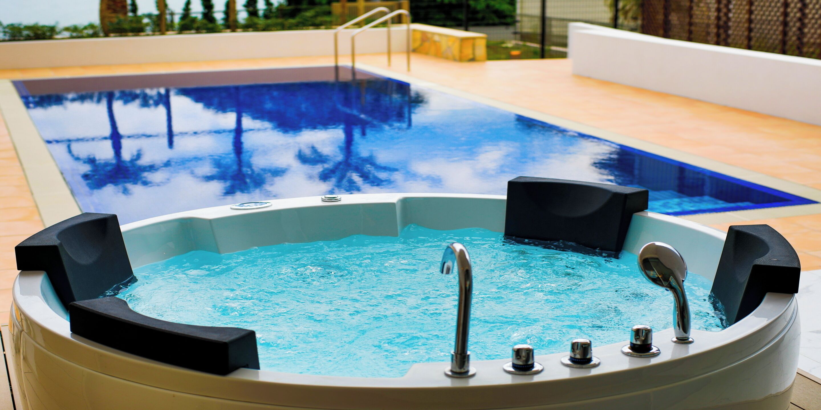 Un bain à remous avec une piscine en arrière-plan, le tout entouré d’une terrasse en bois.