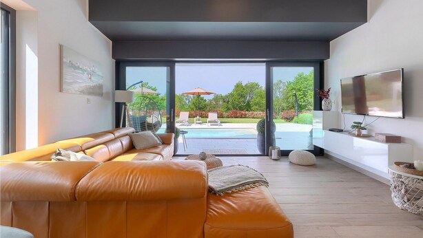 A modern living room with a leather sofa, a flat-screen TV, and a view of a swimming pool and garden. - Awesome home in Sveti Petar u Sumi (Sveti Petar u Sumi)