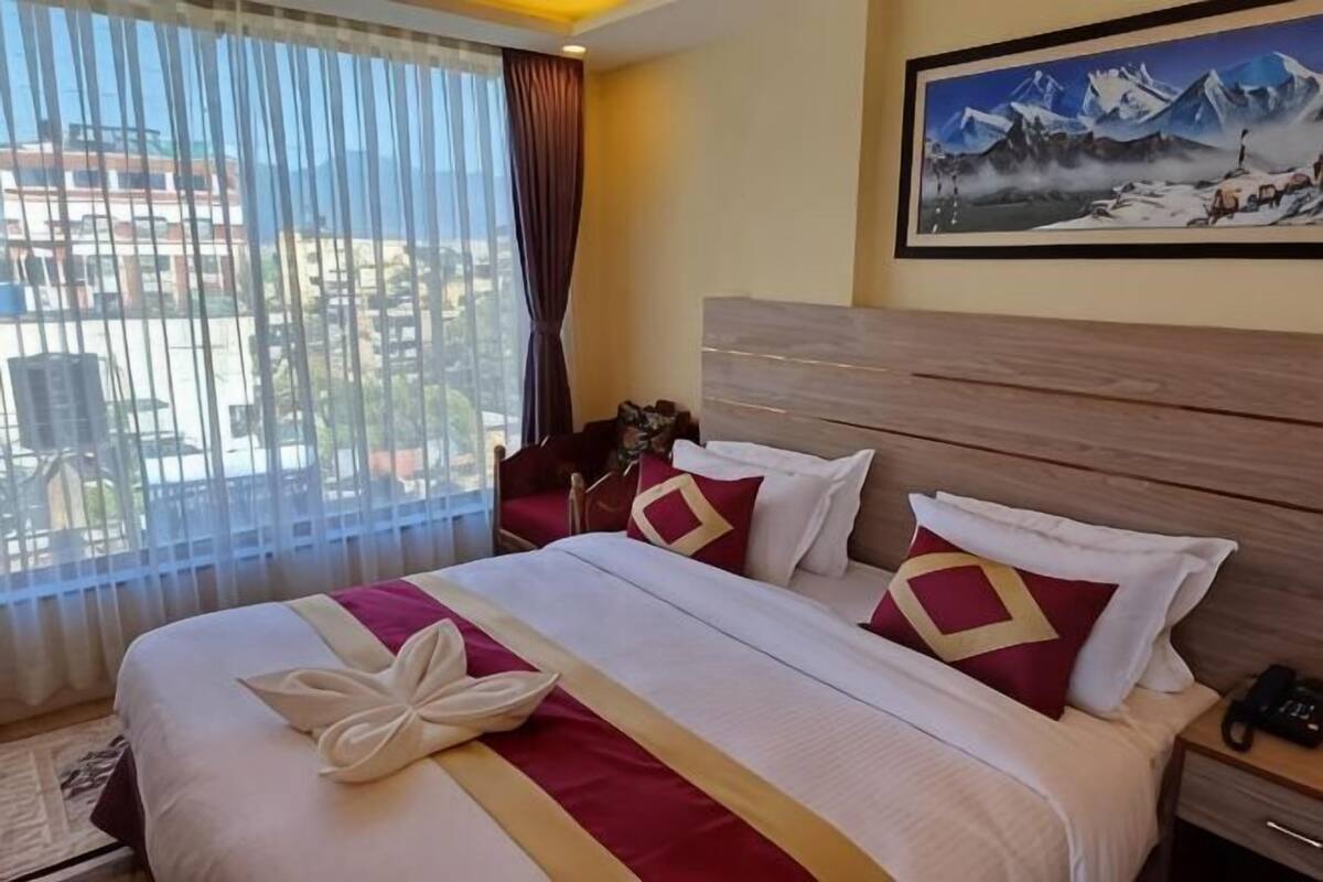 A hotel room with a large bed, a painting on the wall, and a view through the window.