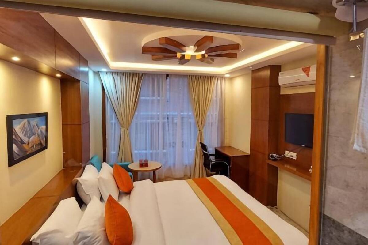 A hotel room with a bed, a desk, a chair, a TV, and a window with curtains.