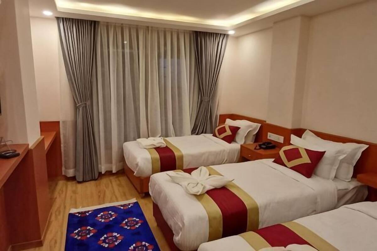 A hotel room with two beds, a desk, and a large window with curtains.