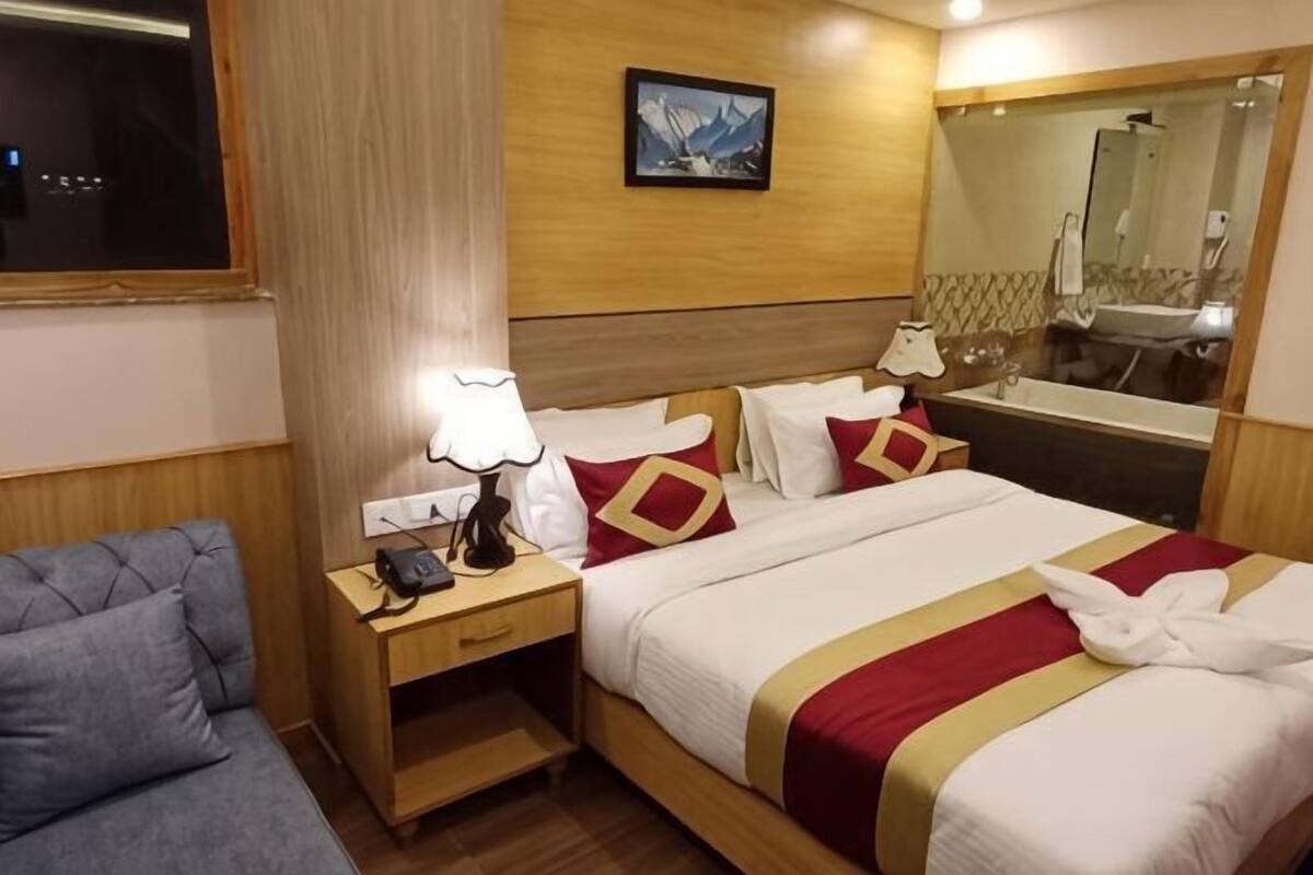 A hotel room with a bed, a bedside table with a lamp, a chair, a mirror, and a painting on the wall.