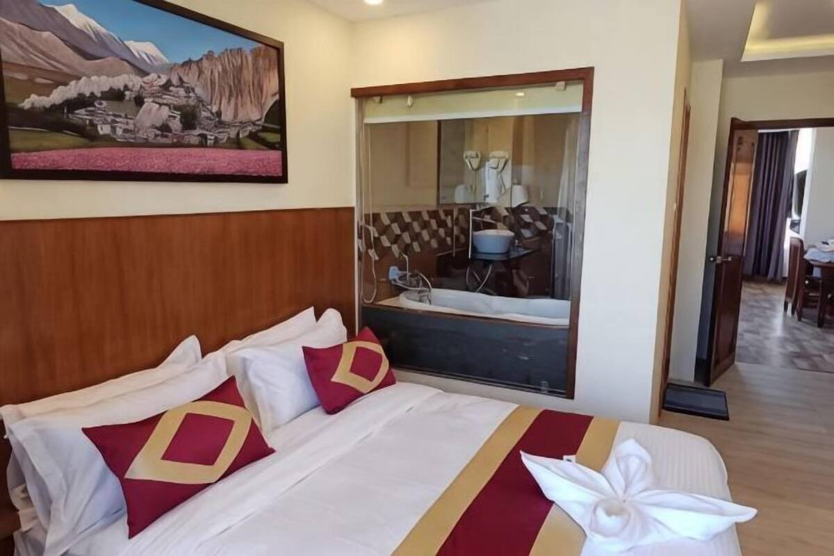 A hotel room with a bed, a large mirror, a bathroom with a bathtub, and a dining area.