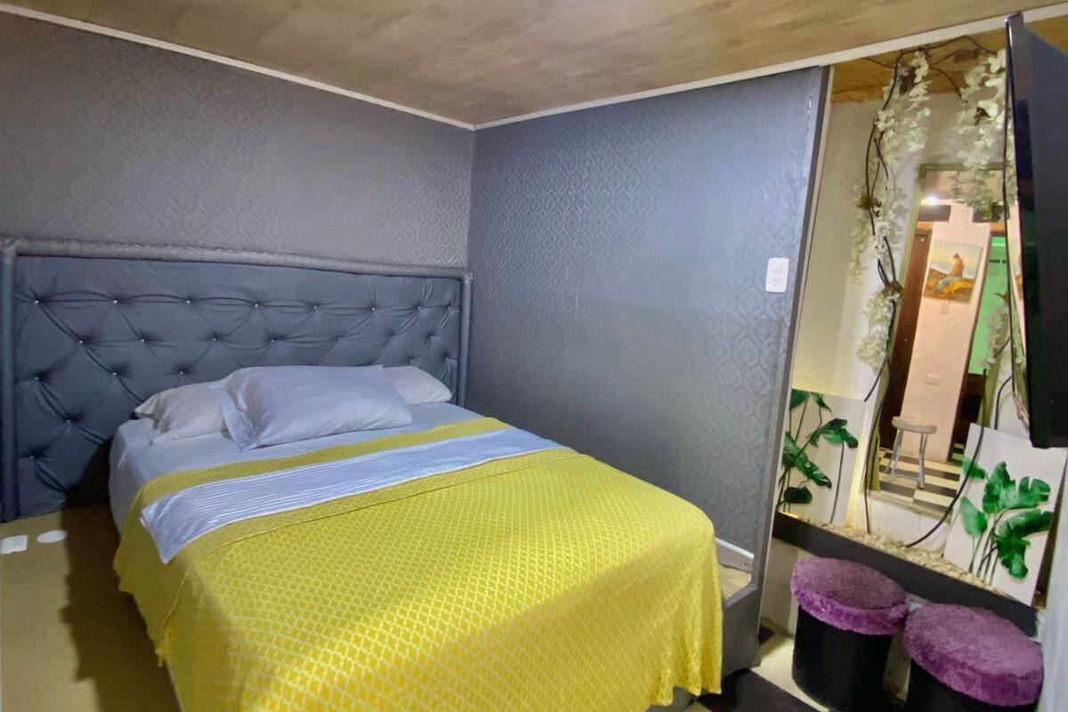 Ein Schlafzimmer mit Bett, Schachbrettmuster-Boden, Spiegel und einer Tür mit Pflanze.