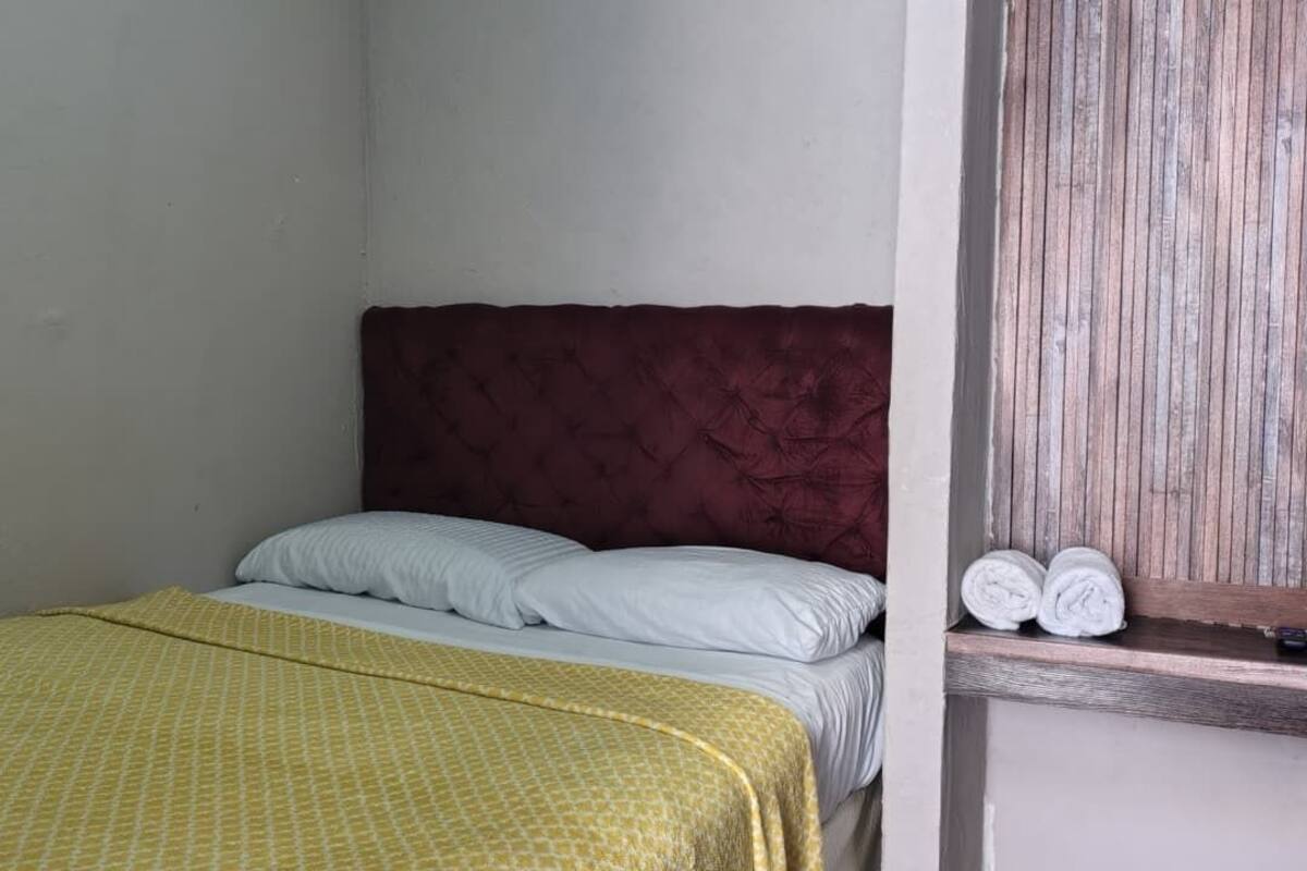 Ein Einzelbett mit Kopfstütze, einer gelben Bettdecke mit Muster und zwei Kissen.