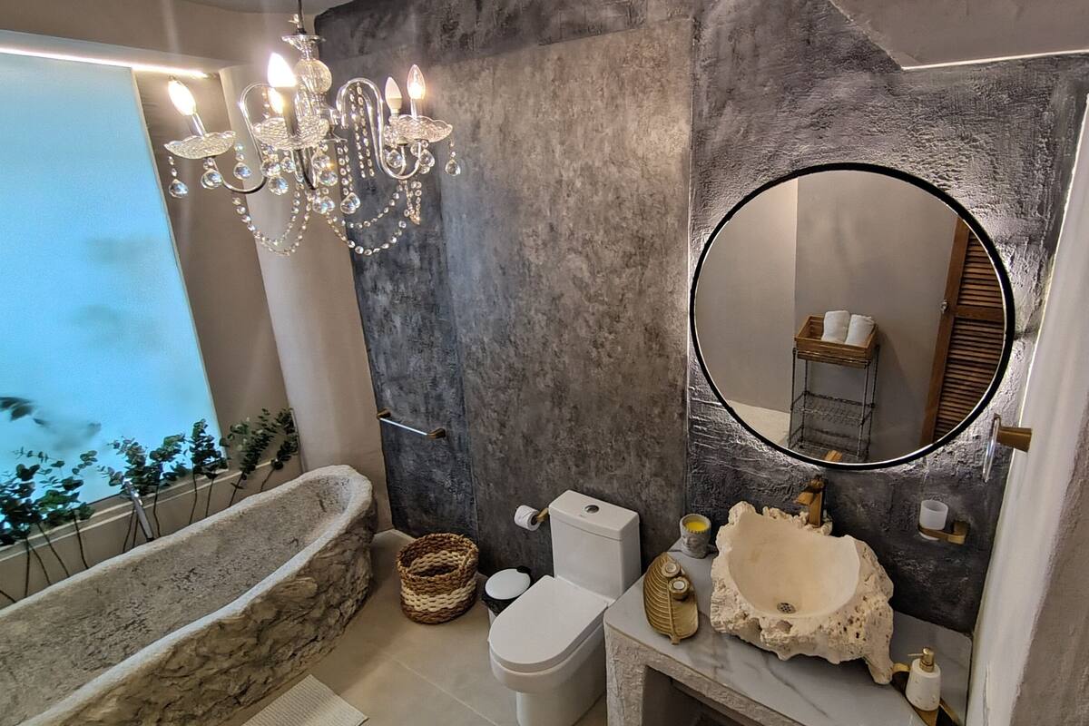 Ein Badezimmer mit einer freistehenden Badewanne, einer Toilette, einem Waschbecken mit dekorativer Steinschale, einer Kristallleuchtreife und einem großen Spiegel.