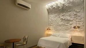 Ein Schlafzimmer mit Bett, Stuhl, Tisch und einer Wand mit Struktur.