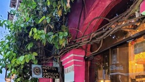 Ein Hostel namens 'HOSPEL LA ANTIGUA' mit einer lebhaften rosa Fassade, einem Schild und einem Fenster, das eine Speisekarte zeigt.