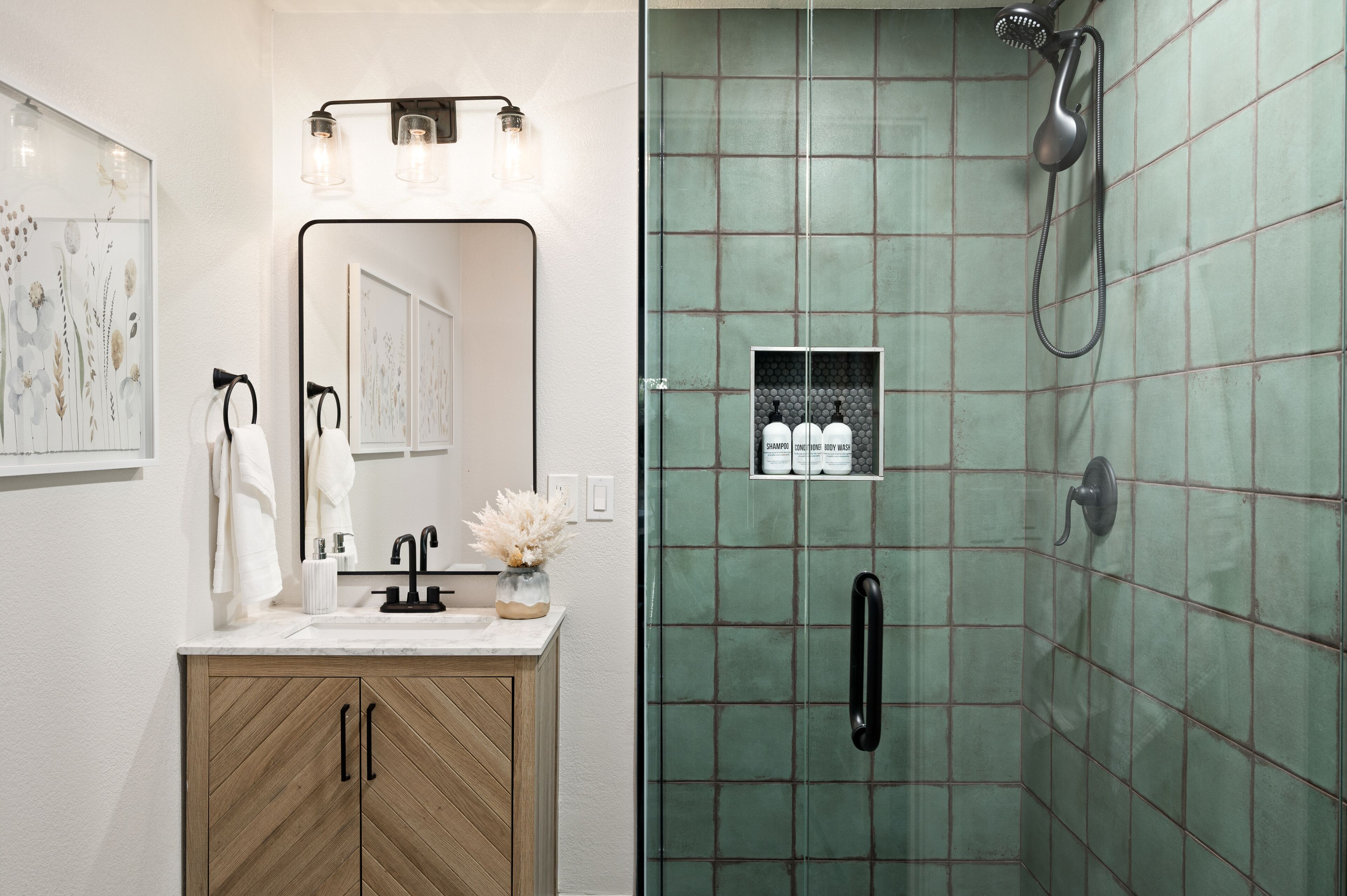 A bathroom with a wooden vanity, a mirror, a sink, and a shower with green tiles.