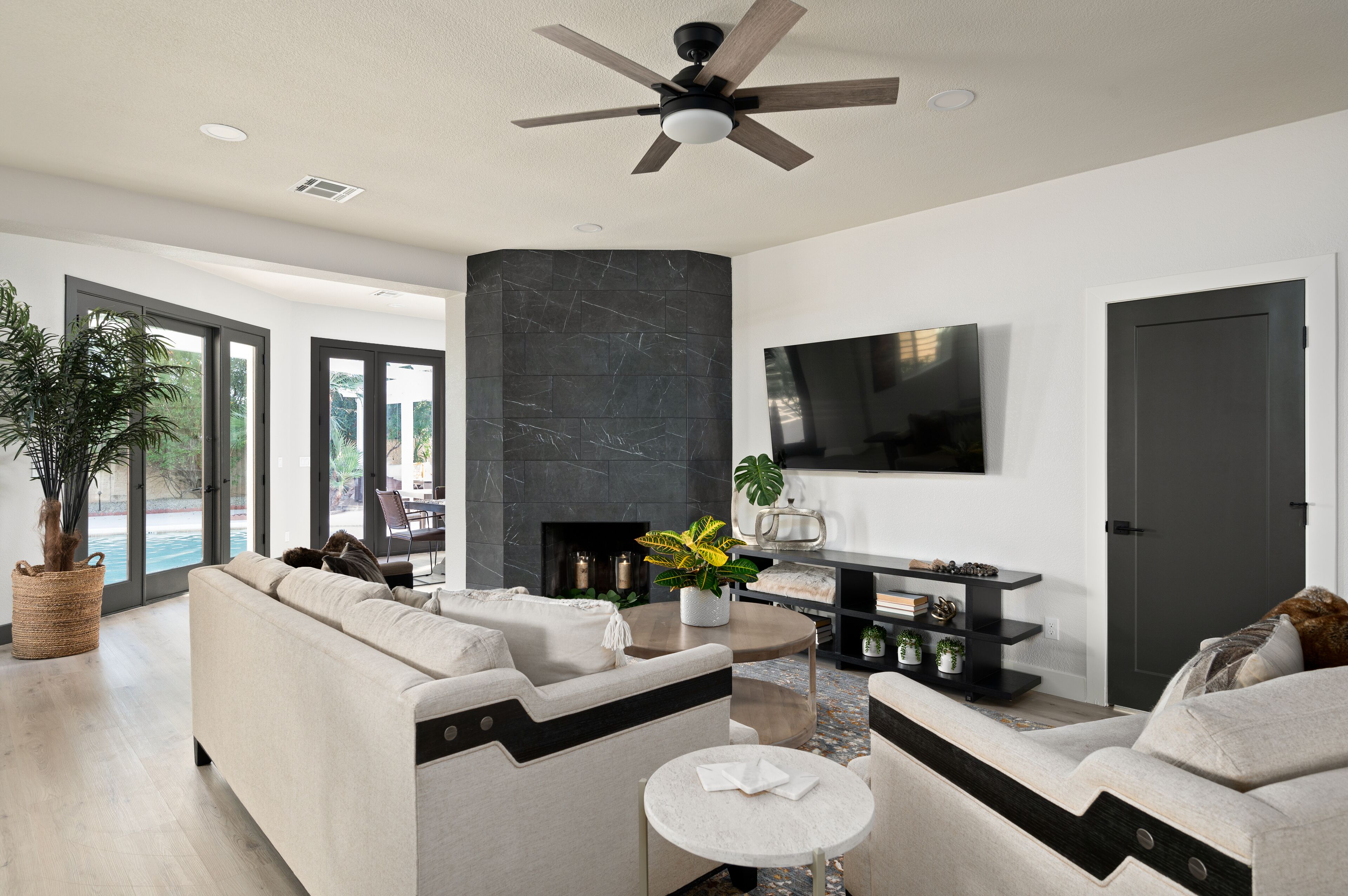 A modern living room with a fireplace, a ceiling fan, and a flat-screen TV mounted on the wall.