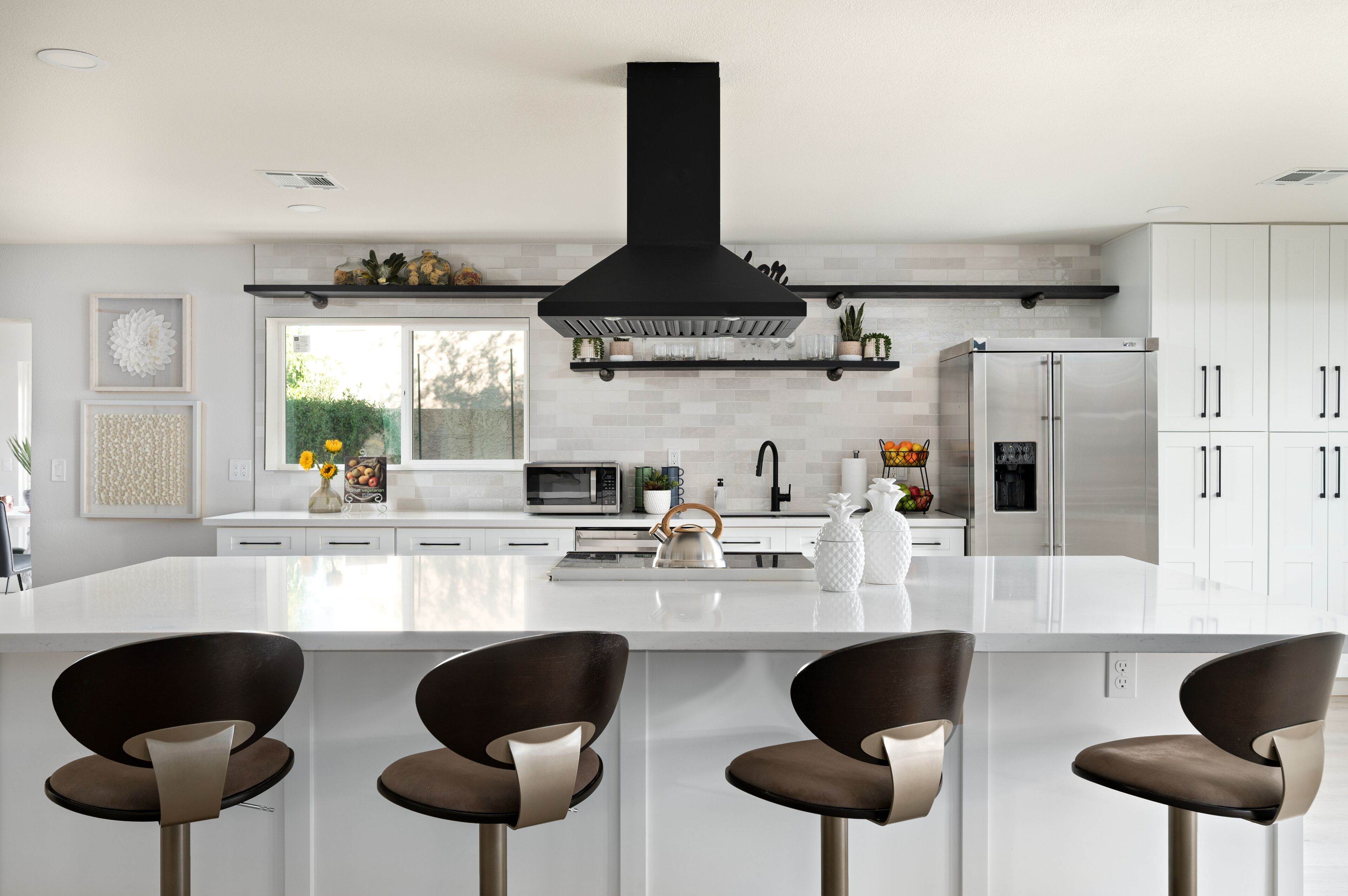 A modern kitchen with a large island, stainless steel appliances, and a black range hood.