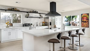 Una cucina moderna con mobili bianchi, una grande isola con sgabelli da bar, un frigorifero in acciaio inossidabile e una cappa aspirante nera.