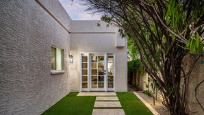 Una casa moderna con facciata bianca, ingresso con porta in vetro, un piccolo prato e un vialetto in pietra che conduce alla porta.