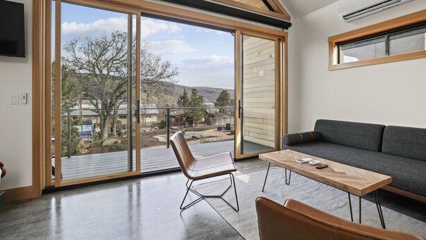A modern living room with a large sliding glass door leading to a balcony, a sofa, a wooden coffee table, and a chair. - CAMP RANDONNEE__CABIN 4 (Mosier)
