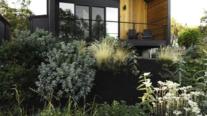 A modern house with a large balcony, surrounded by lush greenery and tall grasses. - CAMP RANDONNEE__CABIN 4 (Mosier)