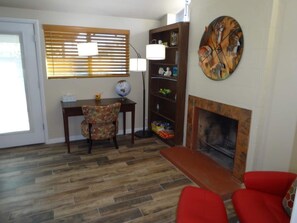 Ein Wohnzimmer mit Kamin, einem roten Sofa, Holzboden, Schreibtisch mit Stuhl, Bücherregal und Globus.