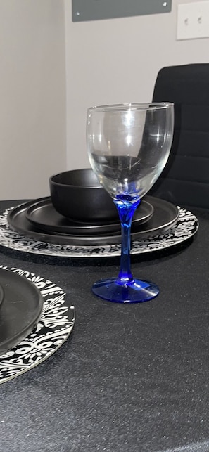 Une table avec un verre bleu, un bol noir et une assiette noire ornée d’un motif blanc.