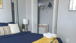 A bedroom with a large bed, a bedside lamp, a crib, and a wardrobe. - King Bed. Funny Bone, Fraze, WPAFB, museum Adventure Reef. Fun get away!  (Kettering)