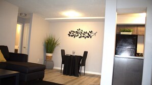 A compact living space with a dining area, a black sofa, a potted plant, and a kitchen area with a refrigerator. - King Bed. Funny Bone, Fraze, WPAFB, museum Adventure Reef. Fun get away!  (Kettering)