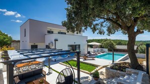 Une maison moderne dotée d’une piscine, d’un espace salon extérieur et d’un grand arbre.