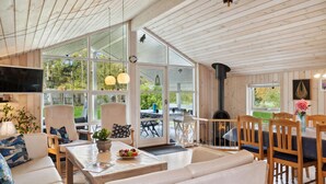 Un interior acogedor con techo de madera, ventanas amplias, chimenea y asientos confortables.