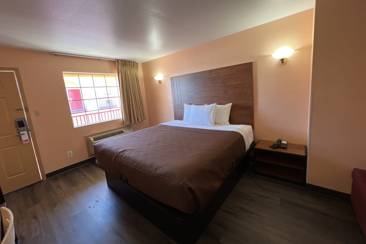 A hotel room with a large bed, a window with curtains, a bedside table, and a wall-mounted light.