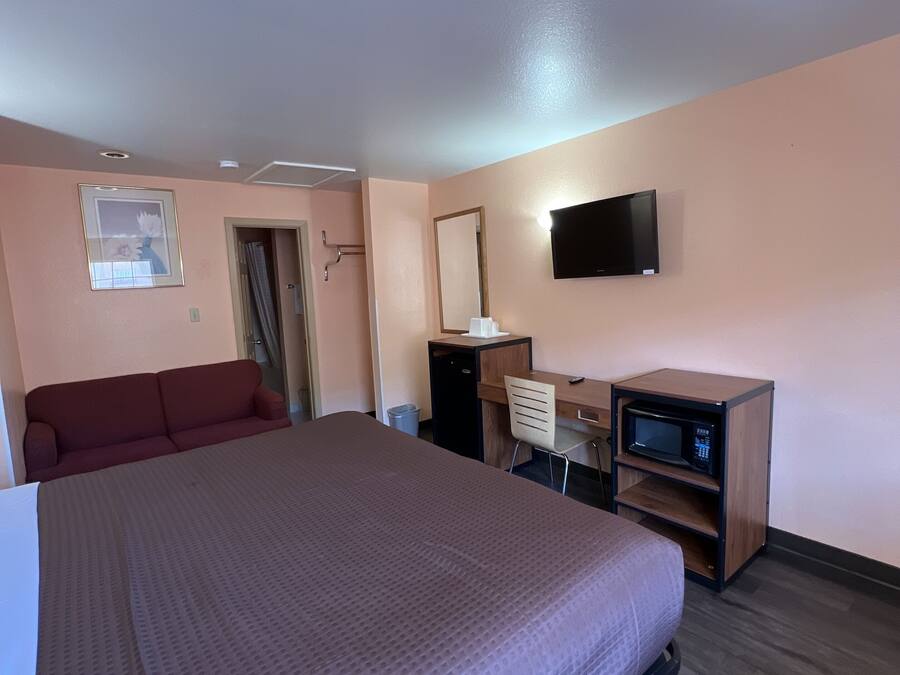 A hotel room with a bed, a desk with a computer, a TV, a microwave, and a red sofa.