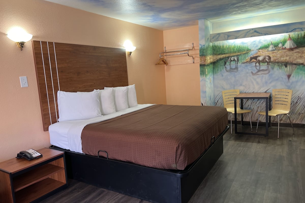 A hotel room with a bed, a small table with chairs, a phone on a side table, and a mural on the wall.