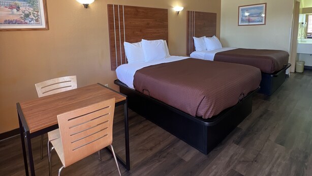 Habitación de hotel con un escritorio de madera, dos camas con ropa de cama marrón y una lámpara de pared.