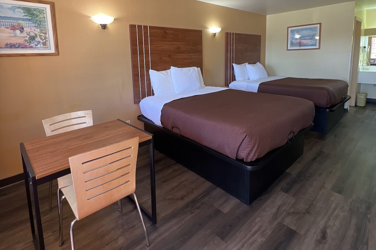 A hotel room with a wooden desk, two beds with brown bedding, and a wall-mounted light fixture.