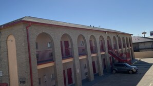 Un edificio con una hilera de arcos y balcones, un estacionamiento y un cielo despejado.