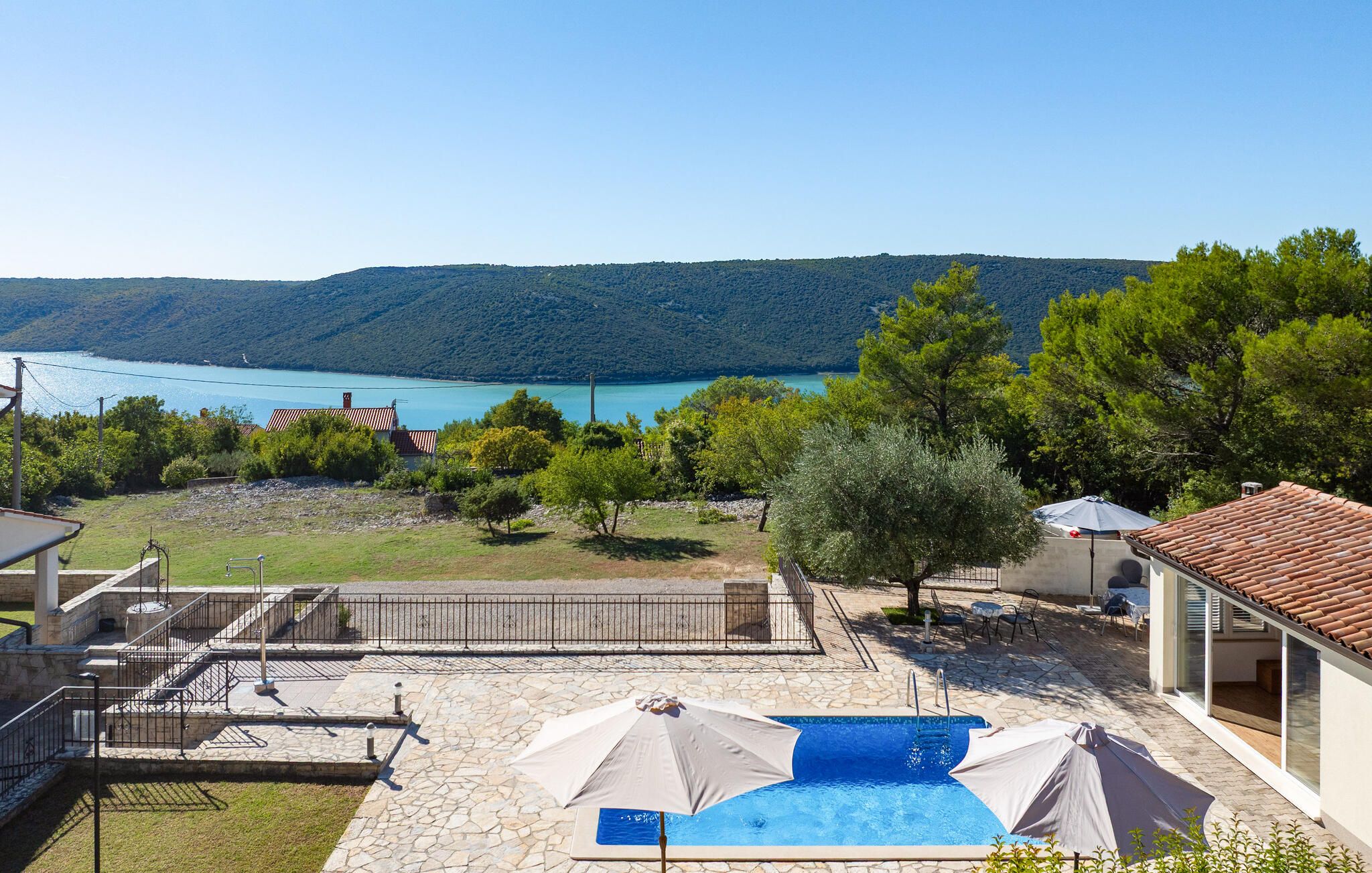 A pool area with a view of a lake and hills, stone steps leading to a building, and outdoor seating.