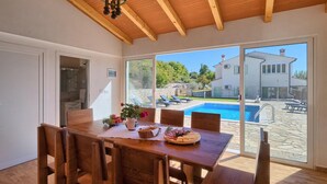 A dining area with a wooden table and chairs, a view of a swimming pool, and a house in the background. - Lovely home in Labin - Rabac (Labin - Rabac)