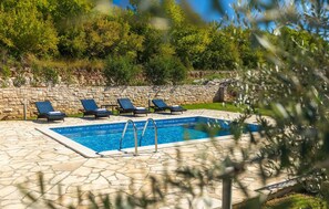 Piscina con baldosas de piedra y cuatro sillas de descanso.