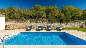 A rectangular swimming pool with a stone border, four lounge chairs, and a stone wall with vegetation behind. - Lovely home in Labin - Rabac (Labin - Rabac)