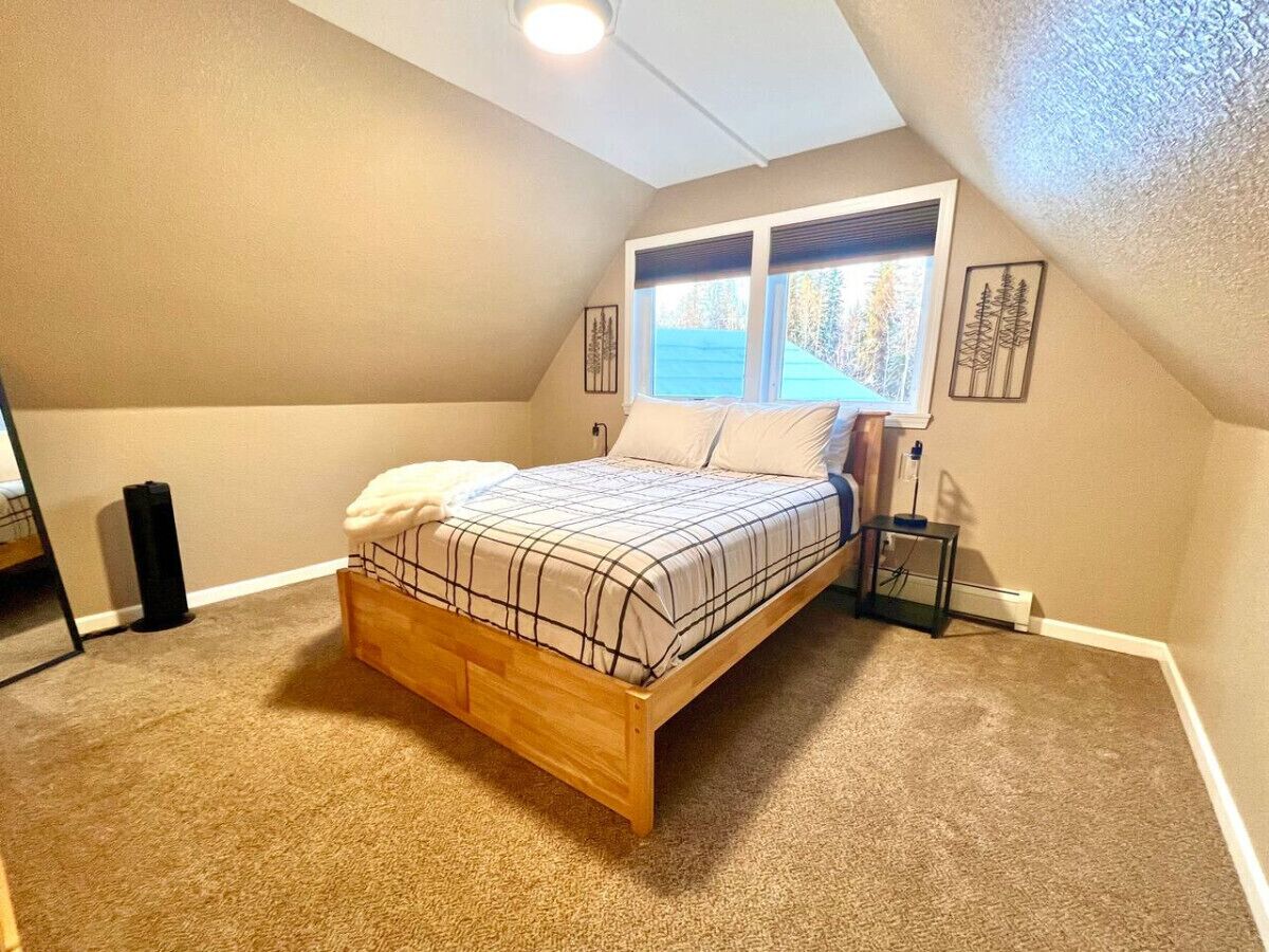 Un dormitorio con cama de madera, paredes color beige, una ventana y una mesita de noche pequeña.