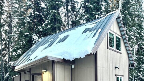 Une petite cabane avec un escalier en bois menant à une porte, entourée de neige et d’arbres.