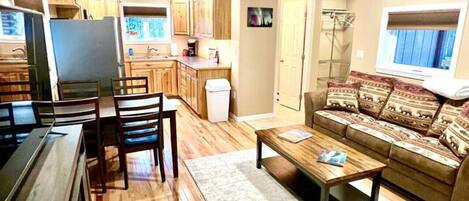 Un amplio salón con piso de madera, un sofá, una mesa de centro y una cocina al fondo.