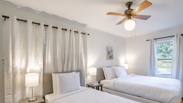 A hotel room with two beds, a ceiling fan, and a window with curtains. - Close to Midtown & Parks - Little Blue (Mobile)