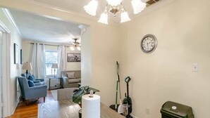 A living room with a sofa, a coffee table, and a chandelier. There is a clock on the wall and a trash can in the corner. - Close to Midtown & Parks - Little Blue (Mobile)