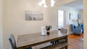 A dining area with a wooden table, chairs, a chandelier, a painting, and a potted plant. - Close to Midtown & Parks - Little Blue (Mobile)