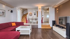 A modern living room with a red sofa, a glass coffee table, a TV, and a staircase leading to a dining area. - Awesome home in Kostrena (Kostrena)