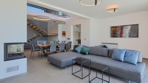 Un espace de vie moderne comprenant un canapé d’angle gris, un coin repas, un escalier et un tableau accroché au mur.