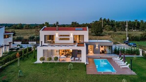 Une maison moderne à deux étages, dotée d’une piscine, d’un espace salon extérieur et d’une pelouse bien entretenue.