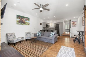 A modern living room with a grey sofa, patterned armchairs, a wooden floor, and a ceiling fan.