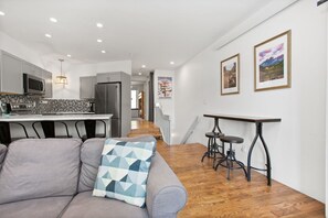 A modern kitchen with grey cabinets, a microwave, and a refrigerator. There is a dining area with a grey sofa and a patterned pillow.