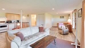 A living room with a white sofa, a wooden coffee table, and a kitchen in the background. - Maine Retreat w/ Ocean Views, Walk to Downtown! (Eastport)