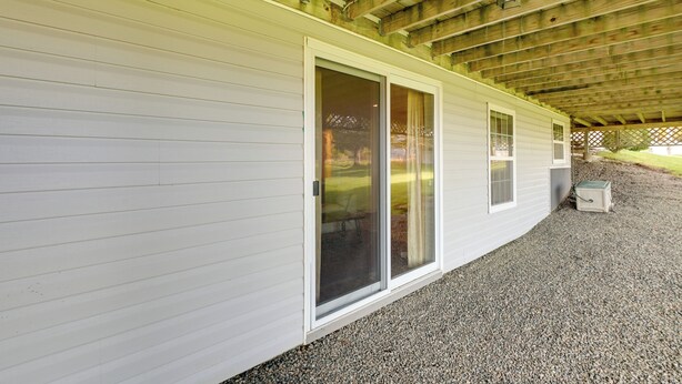 A building with a covered porch, a sliding glass door, and a gravel driveway. - Maine Retreat w/ Ocean Views, Walk to Downtown! (Eastport)