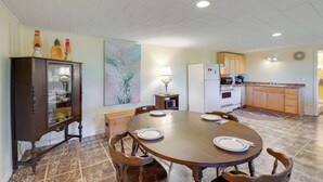 A dining area with a wooden table and chairs, a cabinet with glass doors, and a kitchen in the background. - Maine Retreat w/ Ocean Views, Walk to Downtown! (Eastport)